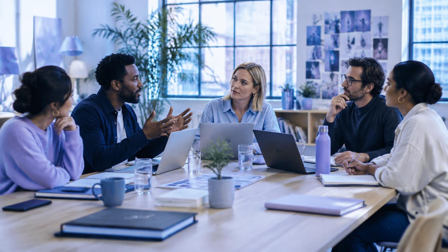 Five agency colleagues discussing strategy around a conference table in a bright studio.